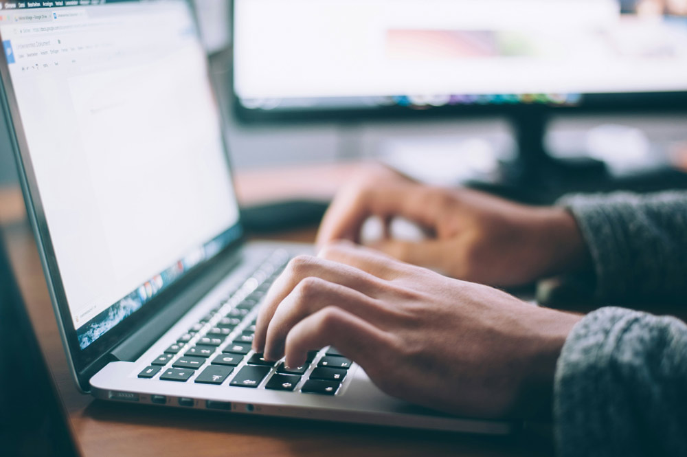 A person typing on a laptop keyboard, writing a post