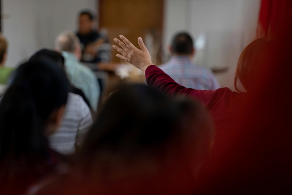 A raised hand in a room of listeners during a public conversation